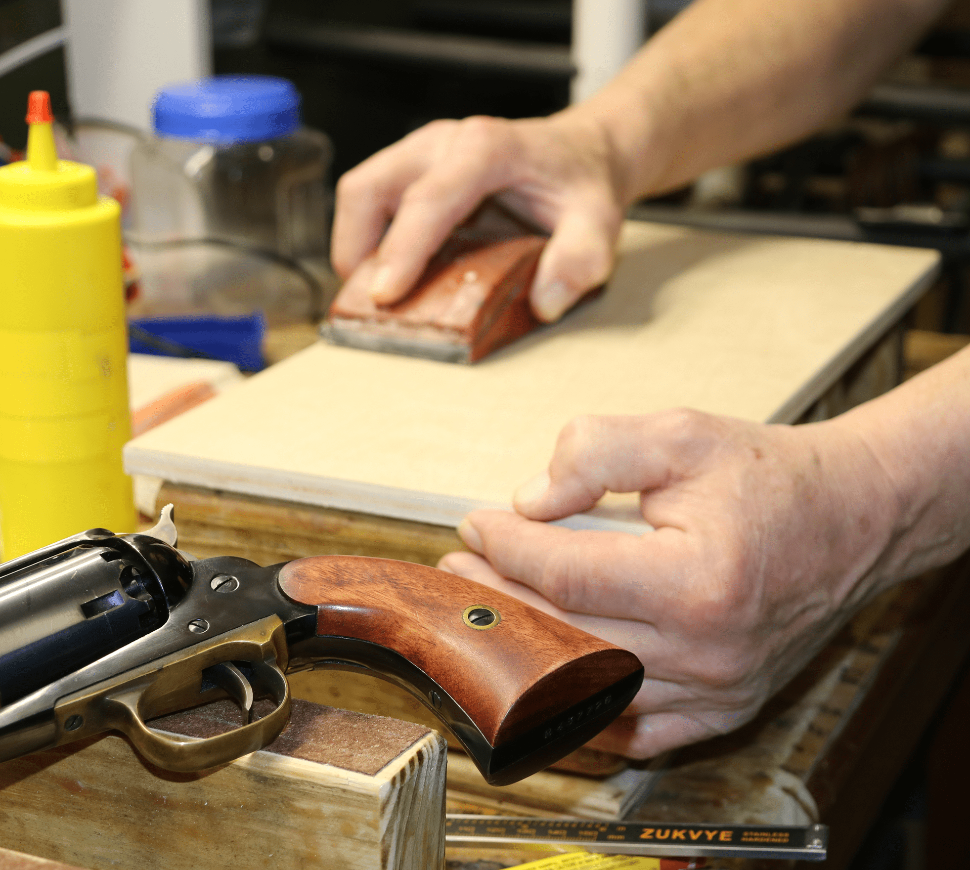 Hands sanding wooden revolver grip on bench